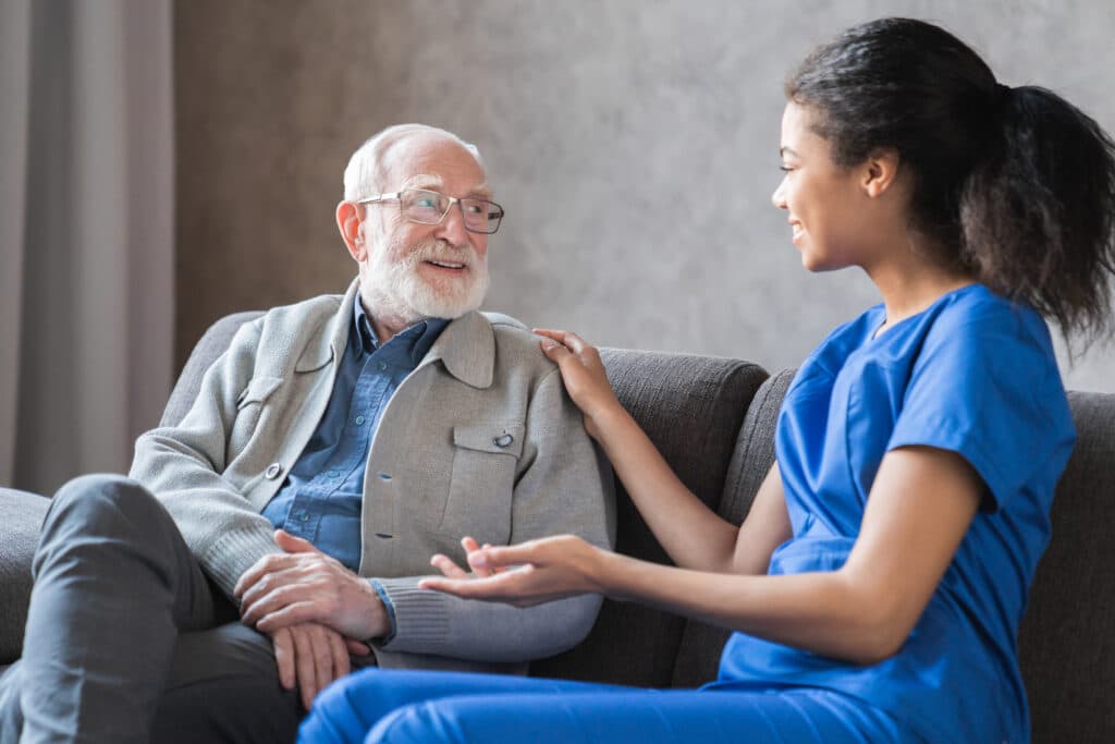 Caring african-american nurse talks to old elderly senior patient holds his hand sit in living room Why the Start of a New Year is the Perfect Time to Review Home Care Services
